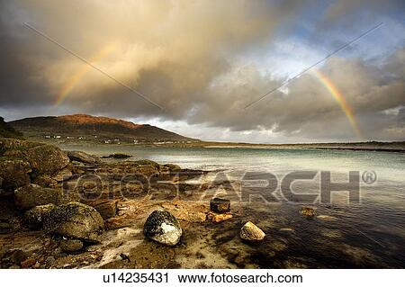Stock Image - Rainbow stretching over still rural lake. Fotosearch