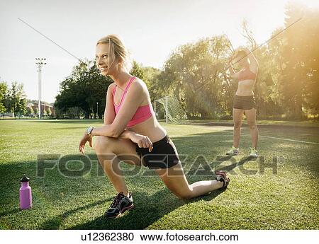 Stock Image - Runners stretching on grass in park. Fotosearch