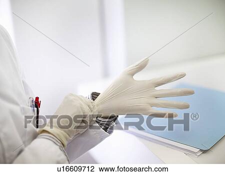 Stock Image - Scientist pulling on latex gloves. Fotosearch