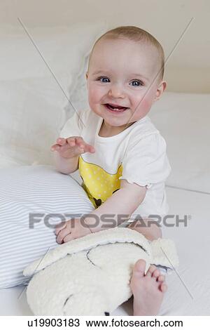 Stock Image - Smiling baby sitting on bed. Fotosearch