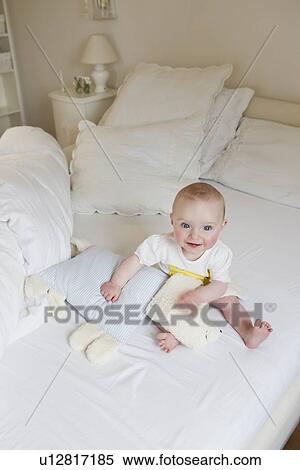 Smiling baby sitting on bed View Large Photo Image Stock Photography - Smiling baby sitting on bed. Fotosearch