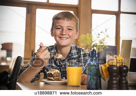Stock Image - Smiling boy eating breakfast at table. Fotosearch