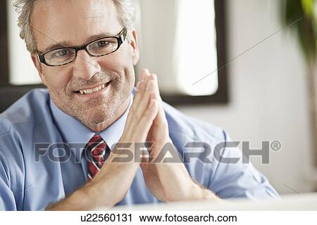 Smiling businessman sitting at desk View Large Photo Image Stock Image - Smiling businessman sitting at desk. Fotosearch