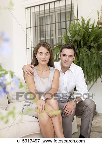 Smiling couple sitting on sofa View Large Photo Image Stock Photo - Smiling couple sitting on sofa. Fotosearch