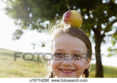 Smiling girl balancing apple on head View Large Photo Image Stock Image - Smiling girl balancing apple on head. Fotosearch