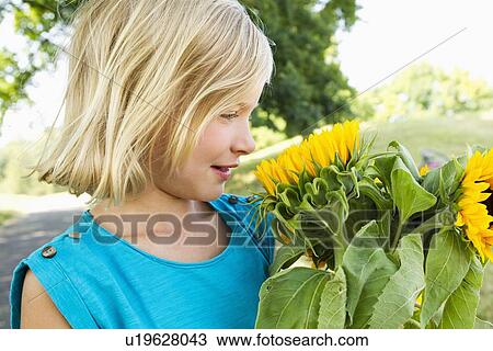 Stock Image - Smiling girl carrying sunflowers. Fotosearch