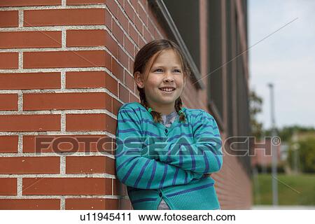 Stock Image - Smiling girl leaning against brick wall. Fotosearch