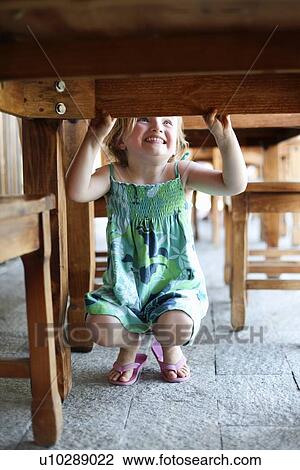 Stock Image - Smiling girl playing under table. Fotosearch