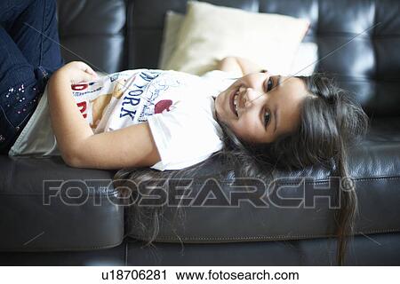 Stock Image - Smiling girl relaxing on sofa. Fotosearch