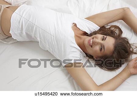 Stock Image - Smiling woman laying on bed. Fotosearch