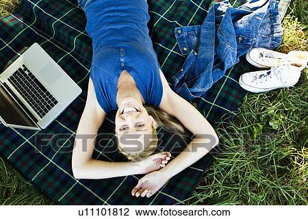 Stock Image - Smiling woman laying on blanket outdoors. Fotosearch