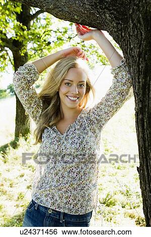 Stock Photograph - Smiling woman leaning on tree. Fotosearch