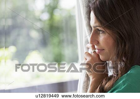 Stock Photo - Smiling woman peering out window. Fotosearch
