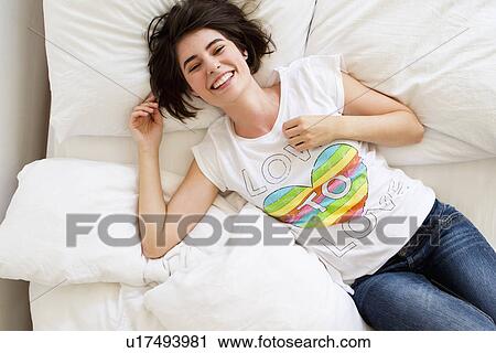 Stock Image - Smiling woman relaxing on bed. Fotosearch