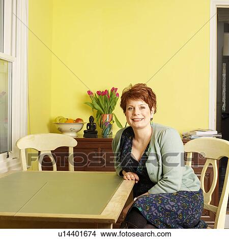 Smiling woman sitting at kitchen table View Large Photo Image Picture - Smiling woman sitting at kitchen table. Fotosearch