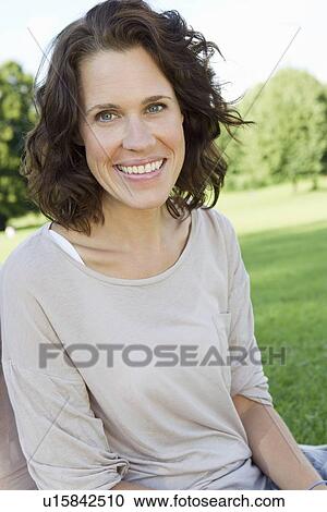 Stock Image - Smiling woman sitting in park. Fotosearch