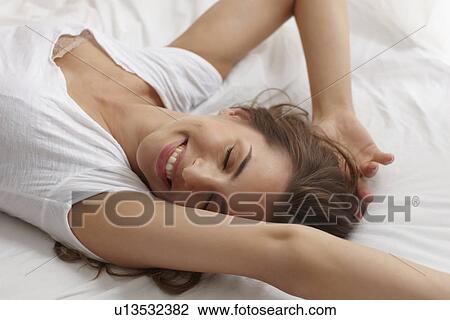 Stock Image - Smiling woman stretching in bed. Fotosearch
