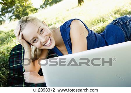 Stock Image - Smiling woman using laptop outdoors. Fotosearch