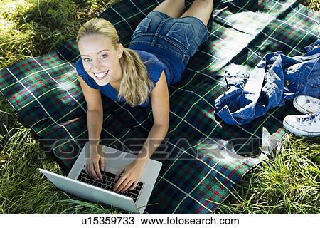 Stock Image - Smiling woman using laptop outdoors. Fotosearch