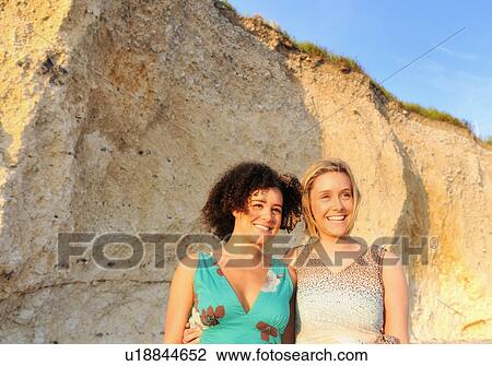 Stock Image - Smiling women standing by cliff. Fotosearch