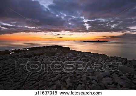 Sun setting over beach rock formations View Large Photo Image Stock Photo - Sun setting over beach rock formations. Fotosearch