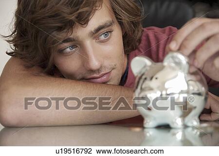 Teenage boy putting money in piggy bank View Large Photo Image Stock Image - Teenage boy putting money in piggy bank. Fotosearch