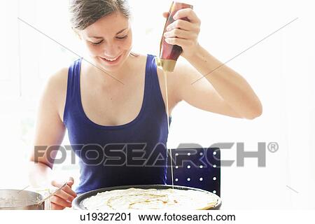 Stock Image - Teenage girl drizzling oil on food. Fotosearch