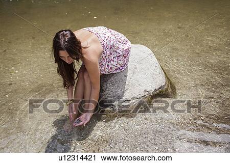 Stock Image - Teenage girl sitting on rock in stream. Fotosearch