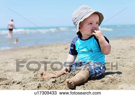 Stock Image - Toddler eating sand on beach. Fotosearch