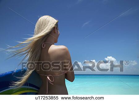 Stock Photography - Woman carrying boogie board on beach. Fotosearch