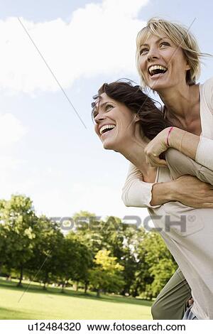 Stock Image - Woman giving her friend a piggy back. Fotosearch