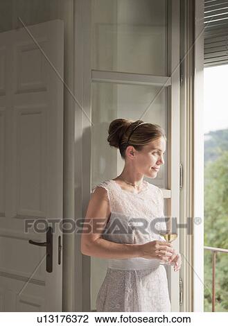 Stock Image - Woman having wine at window. Fotosearch