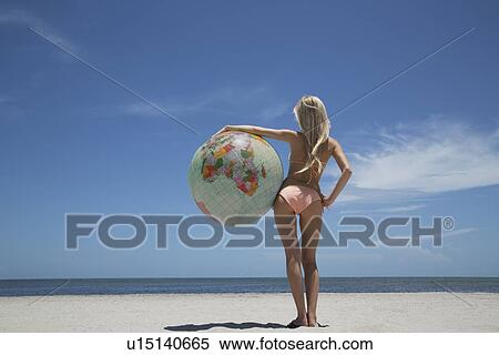 Stock Photography - Woman holding globe on beach. Fotosearch