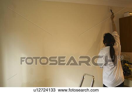 Stock Image - Woman painting trim with paintbrush. Fotosearch
