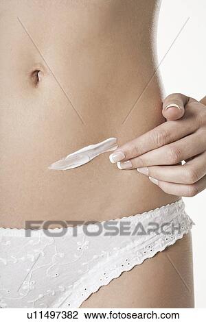 Stock Image - Woman rubbing lotion on belly. Fotosearch