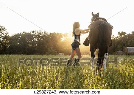 Woman saddling up horse in field View Large Photo Image Stock Image - Woman saddling up horse in field. Fotosearch