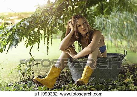 Stock Image - Woman sitting in bucket in garden. Fotosearch