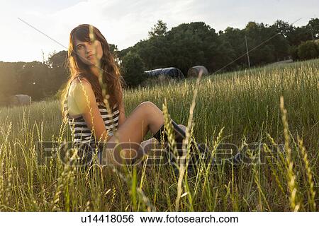 Stock Photograph - Woman sitting in grassy field. Fotosearch