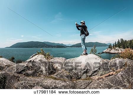 Picture - Woman taking pictures of rural lake. Fotosearch