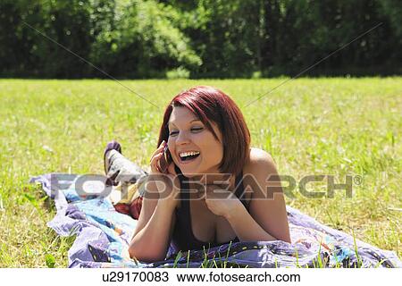 Stock Image - Woman talking on cell phone in grass. Fotosearch