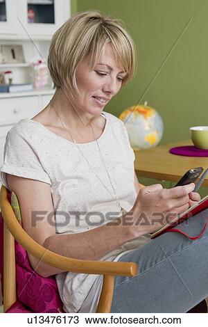 Stock Image - Woman using cell phone in kitchen. Fotosearch