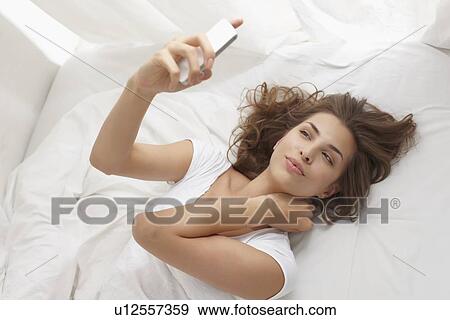 Woman using cell phone on bed View Large Photo Image Stock Photo - Woman using cell phone on bed. Fotosearch