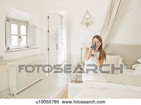 Stock Photography - Woman using video camera in bedroom. Fotosearch
