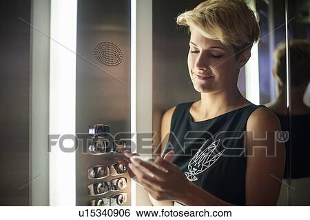 Woman with cell phone in elevator View Large Photo Image Stock Photograph - Woman with cell phone in elevator. Fotosearch