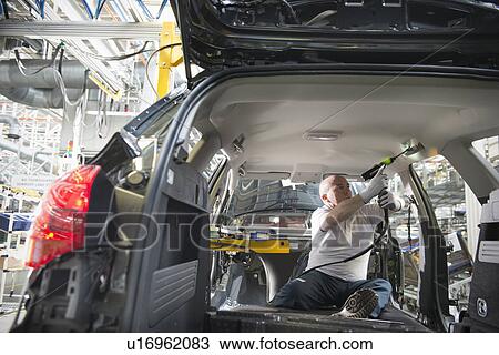 Stock Image - Worker fitting headliner in car in car factory. Fotosearch