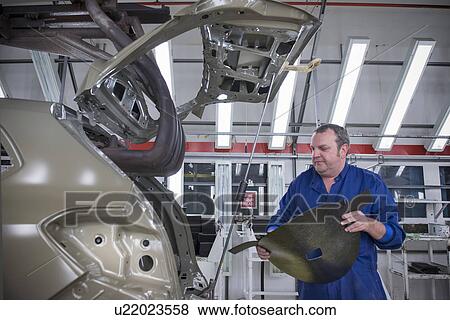 Stock Photo - Worker fitting sound proofing to car in car factory. Fotosearch
