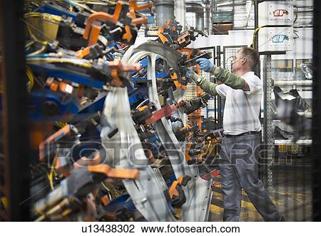 Stock Image - Worker handling car parts in car factory. Fotosearch