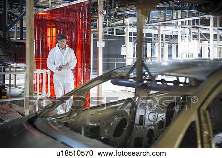 Stock Image - Worker inspecting car body in car factory. Fotosearch