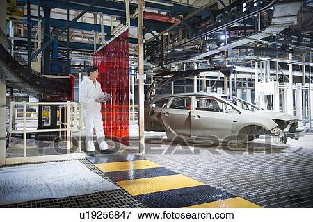 Stock Photo - Worker inspecting car body in car factory. Fotosearch