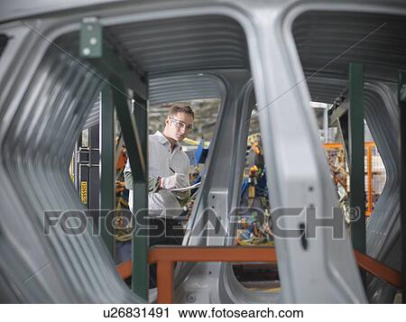 Stock Image - Worker inspecting car parts in car factory. Fotosearch